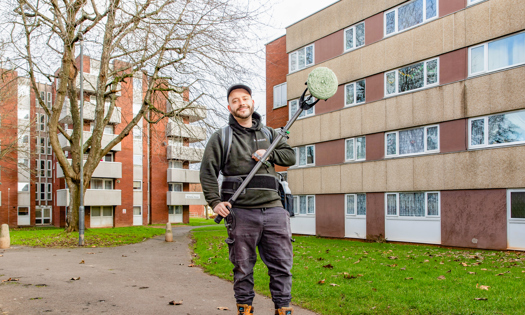 Bromford colleague holding new graffiti removing machine in front of blocks of flats in Bristol