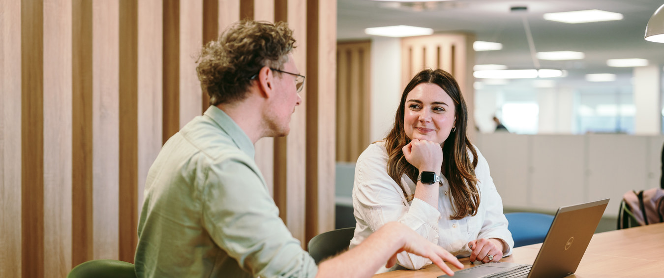 Two people sat at a desk talking