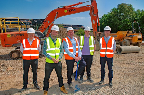 Five Keepmoat and Bromford representatives in hard hats and high vis jackets standing in front of a digger at Park View.
