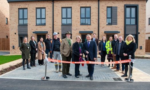 People standing in front of new homes and cutting an opening banner