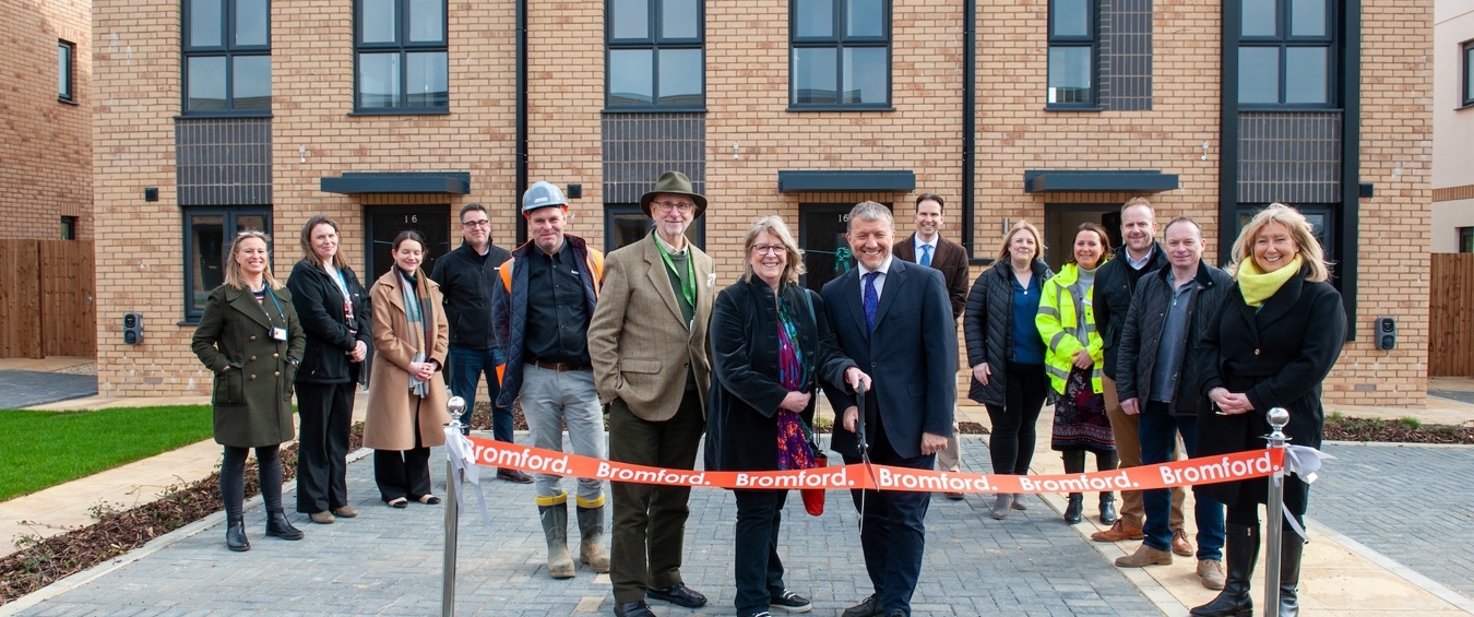 People standing in front of new homes and cutting an opening banner