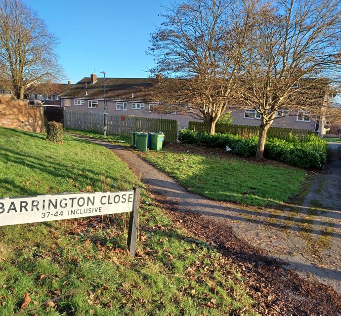 A street sign at Barrington Close with a footpath leading towards some of the homes