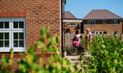 3 people outside a newly built home, two people are standing and a third is sitting in a wheelchair