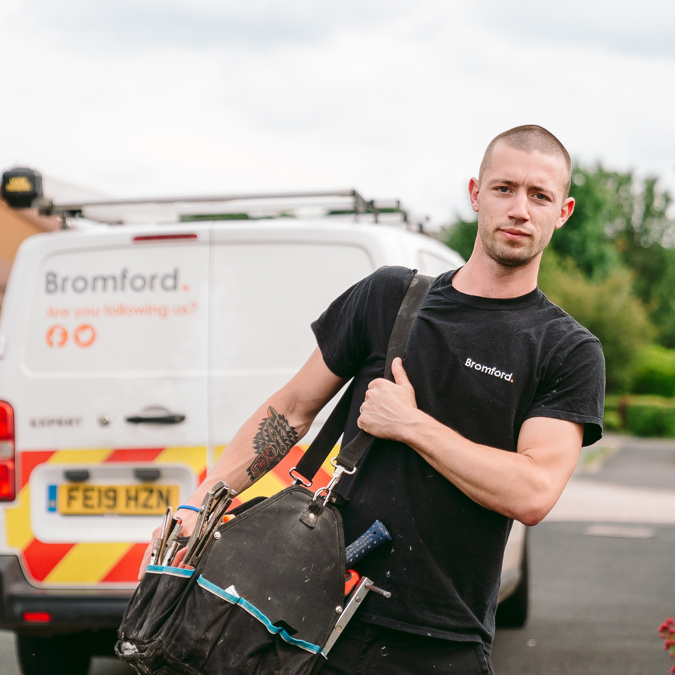 A man walks in front of a parked Bromford van carrying a tool bag