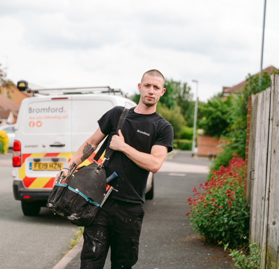 A man walks in front of a parked Bromford van carrying a tool bag