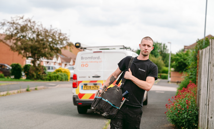 A man walks in front of a parked Bromford van carrying a tool bag