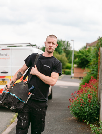 A man walks in front of a parked Bromford van carrying a tool bag