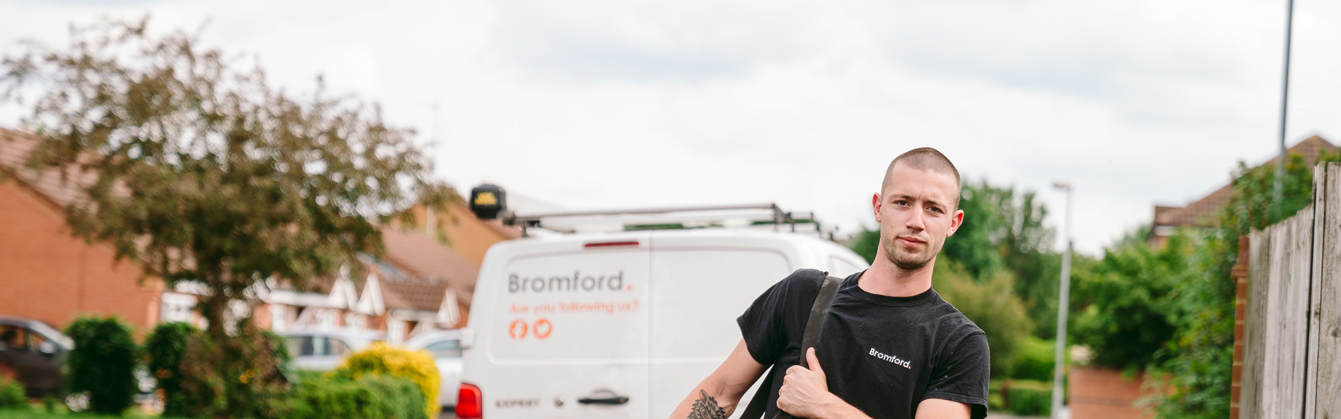 A man walks in front of a parked Bromford van carrying a tool bag