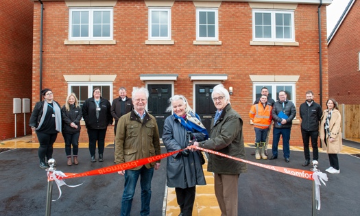 People standing in front of new homes and cutting a opening ribbon 