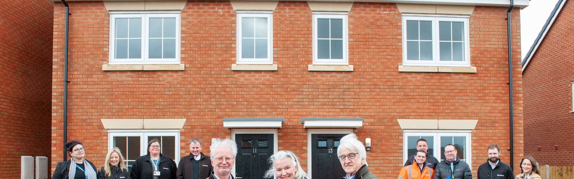 People standing in front of new homes and cutting a opening ribbon 