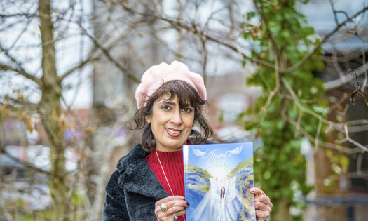 Gina stands outside holding a copy of her book