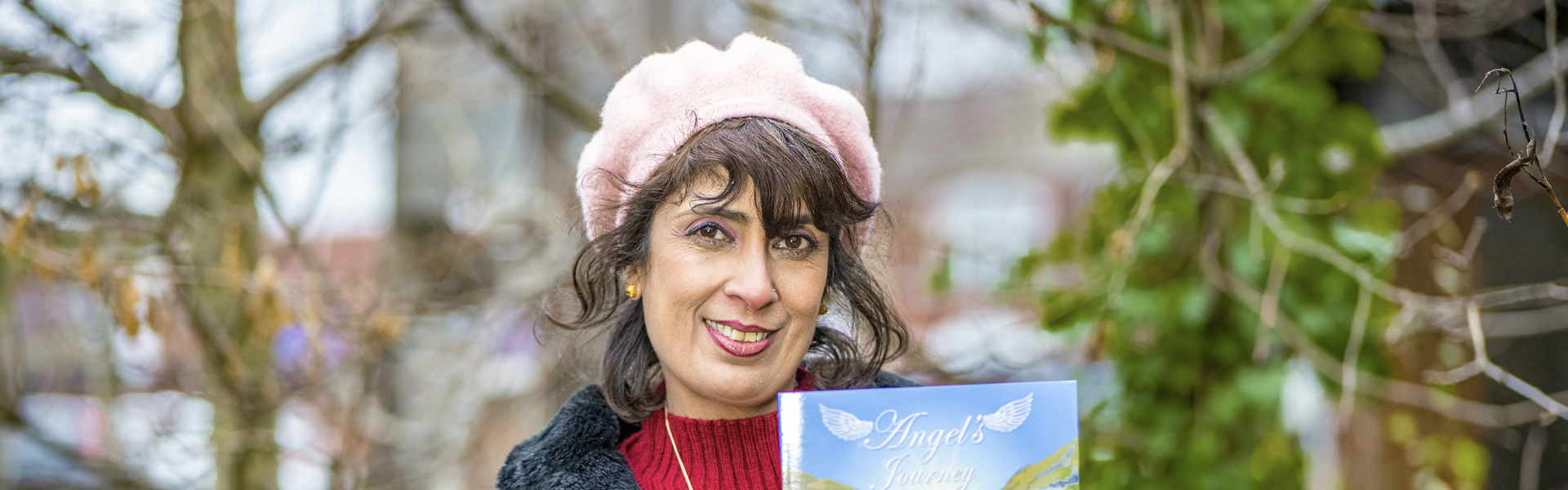 Gina stands outside holding a copy of her book