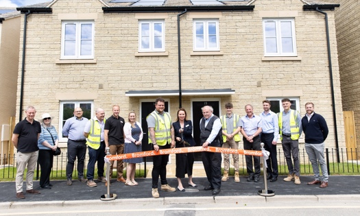 People standing in front of homes and cutting an opening banner