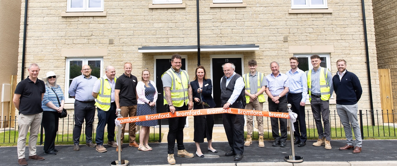 People standing in front of homes and cutting an opening banner