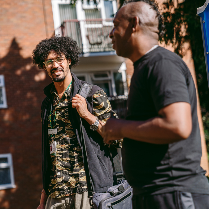 A bromford neighbourhood coach talking to a customer in a communal area in front of some flats