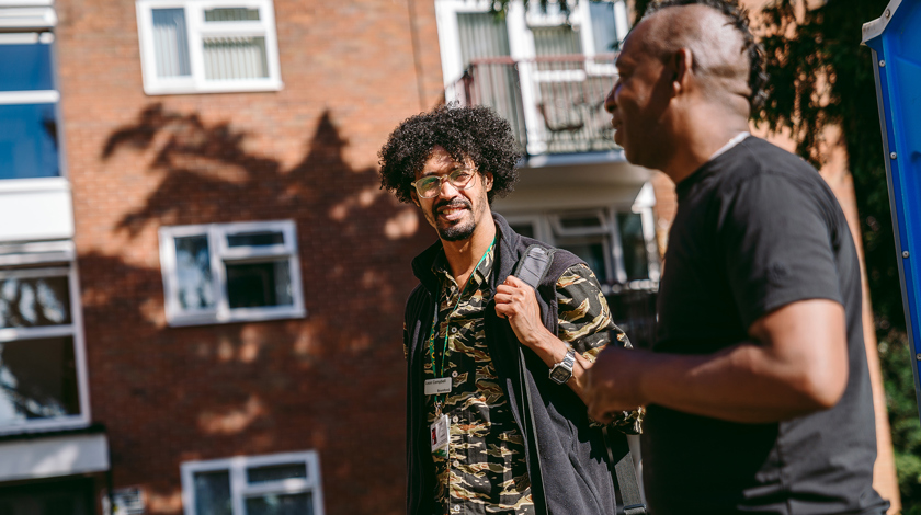 A bromford neighbourhood coach talking to a customer in a communal area in front of some flats